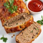 Styled lifestyle food photography of The Best Turkey Meatloaf Recipe served on a white marble table, surrounded by fresh parsley, a small bowl of ketchup glaze, and a side of creamy mashed potatoes, bright airy natural afternoon light, no shadows, no smoke, clean white table, minimal styling, food blog photography style