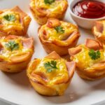 Ham and Cheese Egg Cups served on a white plate with fresh herbs, golden baked tops, and a bright breakfast presentation