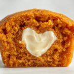 Golden pumpkin cream cheese muffins with cream cheese swirl on a white ceramic plate, white table.