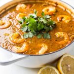 Overhead flat lay of homemade seafood boil sauce in a white bowl on a white marble table, garnished with fresh parsley and lemon wedge