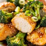Close-up macro shot of easy chicken and broccoli stir fry showing golden chicken interior and bright green broccoli with glossy sauce, sesame seeds visible.