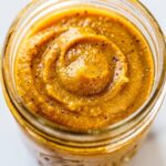 Lifestyle flat lay of pumpkin butter in a glass Mason jar on a white marble table surrounded by warm toast, oatmeal with pumpkin drizzle, cinnamon sticks, nutmeg,