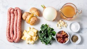 Zuppa Toscana Flat lay of all ingredients for Zuppa Toscana on clean white marble table: Italian sausage, diced potatoes, chopped onion, minced garlic, chicken broth, heavy cream, chopped kale, crumbled bacon, salt and pepper in small bowls, overhead shot