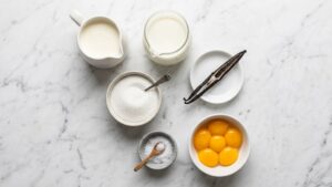 Flat lay of all ingredients for homemade vanilla ice cream on white marble.
