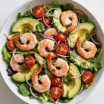 Overhead view of a fresh shrimp and avocado salad with lemon dressing in a white bowl.