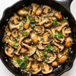 garlic butter mushrooms in a skillet with parsley and glossy butter sauce.