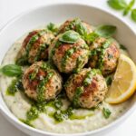 Overhead view of chicken meatballs with pesto white bean puree on a white table