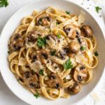 Overhead view of creamy date night mushroom fettuccine with mushrooms, Parmesan, and parsley on a white table.