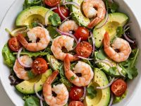 Overhead view of a fresh shrimp and avocado salad with lemon dressing in a white bowl.