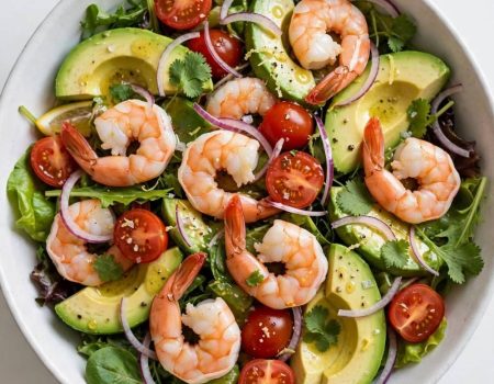 Overhead view of a fresh shrimp and avocado salad with lemon dressing in a white bowl.