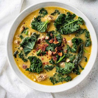 Zuppa Toscana recipe served in a white ceramic bowl overhead flat lay, creamy golden soup with Italian sausage, kale, and crumbled bacon, Parmesan cheese on the side, white marble table, natural daylight