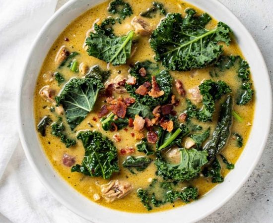Zuppa Toscana recipe served in a white ceramic bowl overhead flat lay, creamy golden soup with Italian sausage, kale, and crumbled bacon, Parmesan cheese on the side, white marble table, natural daylight