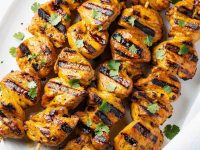 Golden honey chipotle chicken skewers on a white ceramic plate, garnished with fresh cilantro and a small bowl of chipotle sauce on the side, bright natural light on a clean white table.