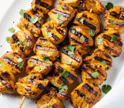 Golden honey chipotle chicken skewers on a white ceramic plate, garnished with fresh cilantro and a small bowl of chipotle sauce on the side, bright natural light on a clean white table.