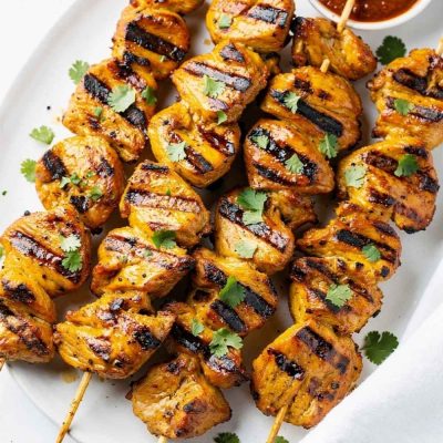 Golden honey chipotle chicken skewers on a white ceramic plate, garnished with fresh cilantro and a small bowl of chipotle sauce on the side, bright natural light on a clean white table.