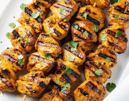 Golden honey chipotle chicken skewers on a white ceramic plate, garnished with fresh cilantro and a small bowl of chipotle sauce on the side, bright natural light on a clean white table.