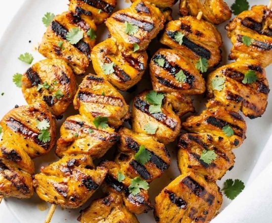 Golden honey chipotle chicken skewers on a white ceramic plate, garnished with fresh cilantro and a small bowl of chipotle sauce on the side, bright natural light on a clean white table.