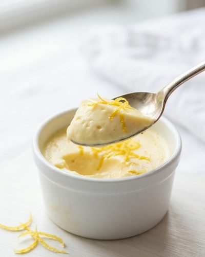 Overhead shot of lemon posset in glass ramekins on a white table.