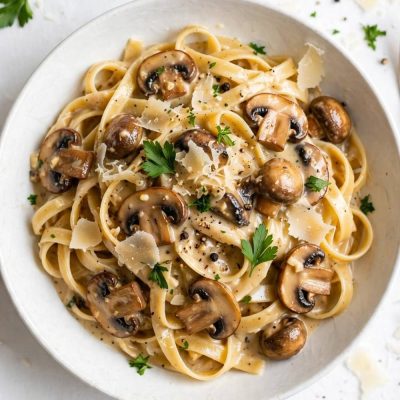 Overhead view of creamy date night mushroom fettuccine with mushrooms, Parmesan, and parsley on a white table.