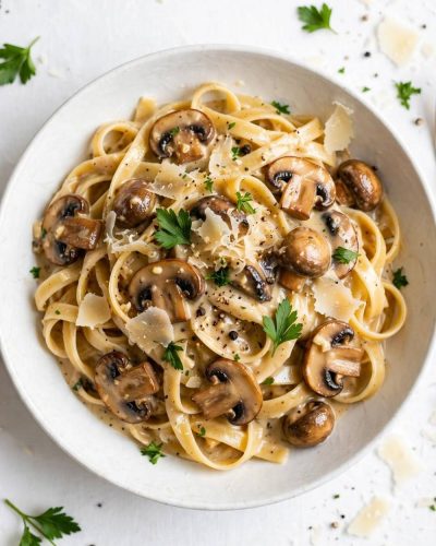 Overhead view of creamy date night mushroom fettuccine with mushrooms, Parmesan, and parsley on a white table.