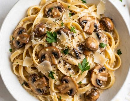 Overhead view of creamy date night mushroom fettuccine with mushrooms, Parmesan, and parsley on a white table.