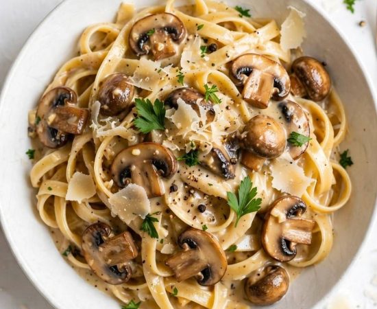 Overhead view of creamy date night mushroom fettuccine with mushrooms, Parmesan, and parsley on a white table.