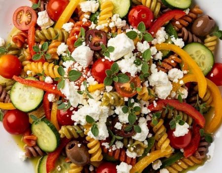 Overhead flat lay of quick and easy pasta salad on white ceramic plate with feta and fresh basil