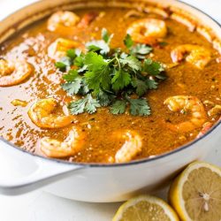 Overhead flat lay of homemade seafood boil sauce in a white bowl on a white marble table, garnished with fresh parsley and lemon wedge