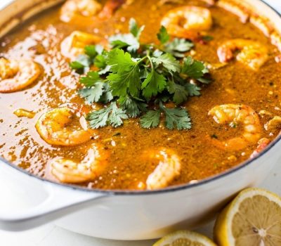 Overhead flat lay of homemade seafood boil sauce in a white bowl on a white marble table, garnished with fresh parsley and lemon wedge