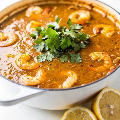 Overhead flat lay of homemade seafood boil sauce in a white bowl on a white marble table, garnished with fresh parsley and lemon wedge