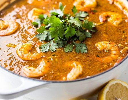 Overhead flat lay of homemade seafood boil sauce in a white bowl on a white marble table, garnished with fresh parsley and lemon wedge