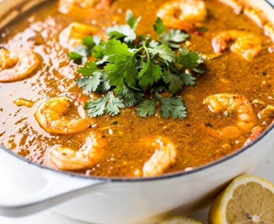 Overhead flat lay of homemade seafood boil sauce in a white bowl on a white marble table, garnished with fresh parsley and lemon wedge