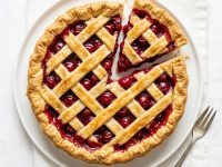 Homemade cherry pie on a white background with a flaky golden crust and glossy cherry filling.