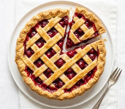 Homemade cherry pie on a white background with a flaky golden crust and glossy cherry filling.