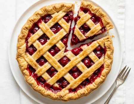 Homemade cherry pie on a white background with a flaky golden crust and glossy cherry filling.