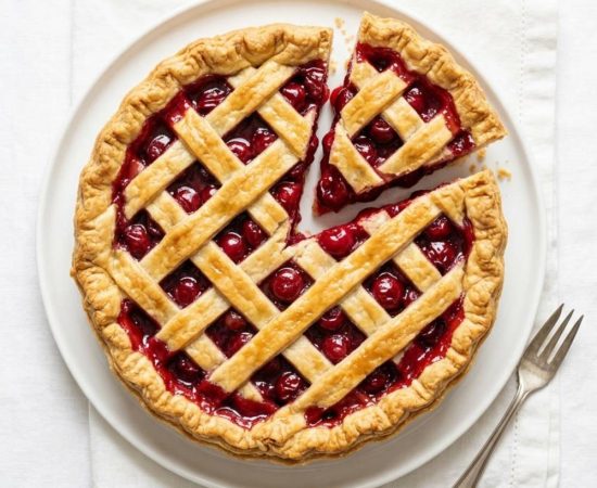 Homemade cherry pie on a white background with a flaky golden crust and glossy cherry filling.
