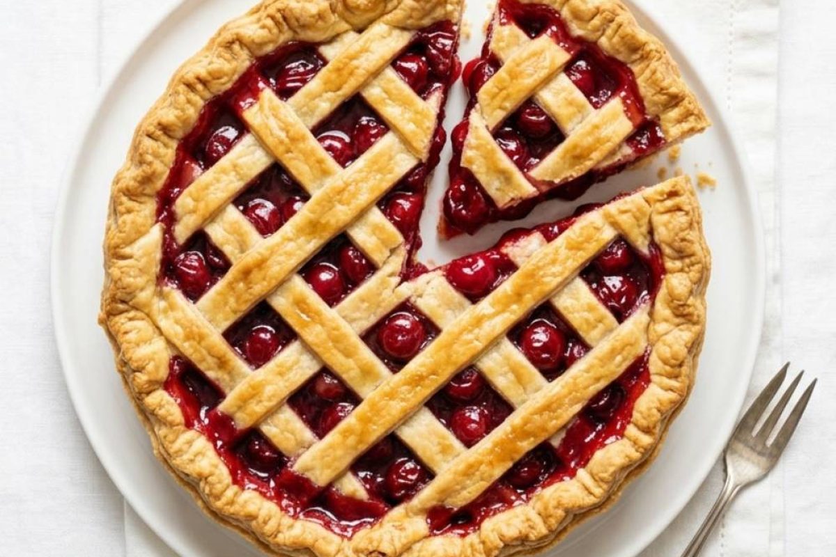 Homemade cherry pie on a white background with a flaky golden crust and glossy cherry filling.