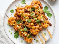 Overhead flat lay of golden bang bang shrimp skewers on a white plate with Bang Bang sauce and cilantro garnish