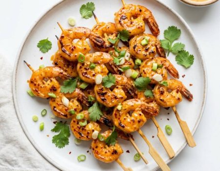 Overhead flat lay of golden bang bang shrimp skewers on a white plate with Bang Bang sauce and cilantro garnish