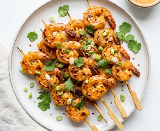 Overhead flat lay of golden bang bang shrimp skewers on a white plate with Bang Bang sauce and cilantro garnish