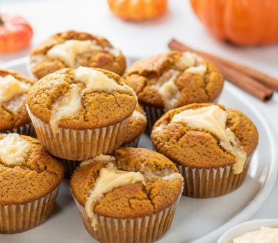 Golden pumpkin cream cheese muffins with cream cheese swirl on a white ceramic plate, white table.