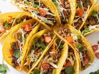 Overhead flat lay of Brandon's Egg Roll Tacos with crispy golden shells, seasoned pork filling, shredded cabbage, carrots, and fresh cilantro on a white table.