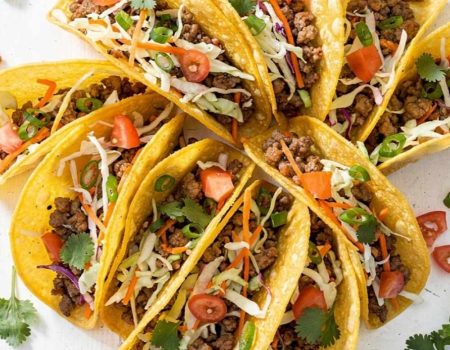 Overhead flat lay of Brandon's Egg Roll Tacos with crispy golden shells, seasoned pork filling, shredded cabbage, carrots, and fresh cilantro on a white table.