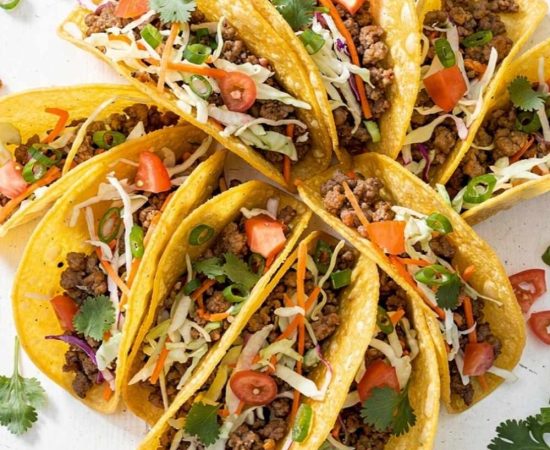 Overhead flat lay of Brandon's Egg Roll Tacos with crispy golden shells, seasoned pork filling, shredded cabbage, carrots, and fresh cilantro on a white table.