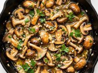 garlic butter mushrooms in a skillet with parsley and glossy butter sauce.
