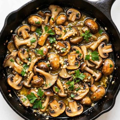 garlic butter mushrooms in a skillet with parsley and glossy butter sauce.