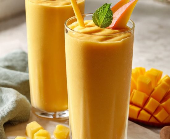 Two tall glasses of tropical fruit smoothie with milk garnished with fresh mango and mint on white marble — best 5-minute blender recipe