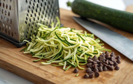 Grating fresh zucchini on a wooden cutting board.