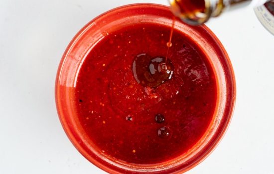 Adding hot sauce and Worcestershire sauce into a bowl of cocktail sauce on a bright white table.