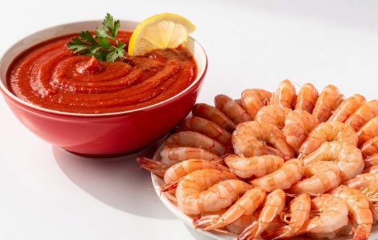 Finished homemade cocktail sauce in a bowl served with fresh shrimp on a bright white table.